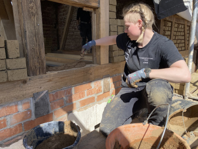 Eine Frau arbeitet an einem Fachwerk-Gefach und baut Lehmsteine ein.