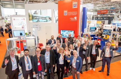 Sicht von oben auf den LEA Hessen Messestand auf der Hannover Messe 2023 mit einer Gruppe von winkenden LEA-Mitarbeitern.