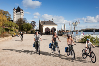 Familie mit zwei Kindern beim Radfahren vor der Kulisse der Stadt Eltville.