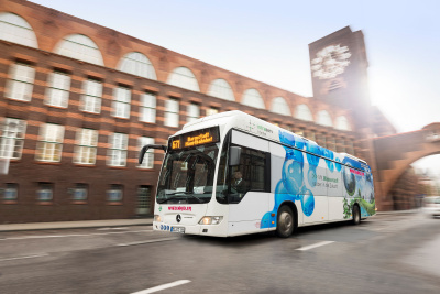 Wasserstoff: H2-Bus Darmstadt H2-Bus der Firma Winzenhöler fährt durch Darmstadt, im Hintergrund ein Gebäude mit Turm und großer Uhr.